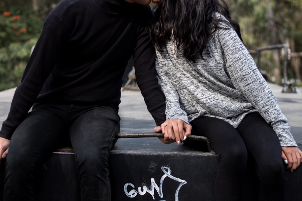 a man and woman sitting on a black garbage can