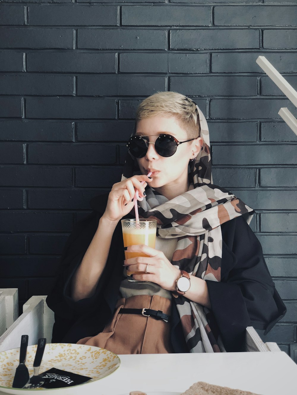 a woman wearing sunglasses and holding a drink