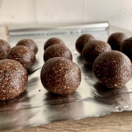 Several chocolate energy balls, textured with visible bits of oats or nuts, arranged on a sheet of aluminum foil with a light background.