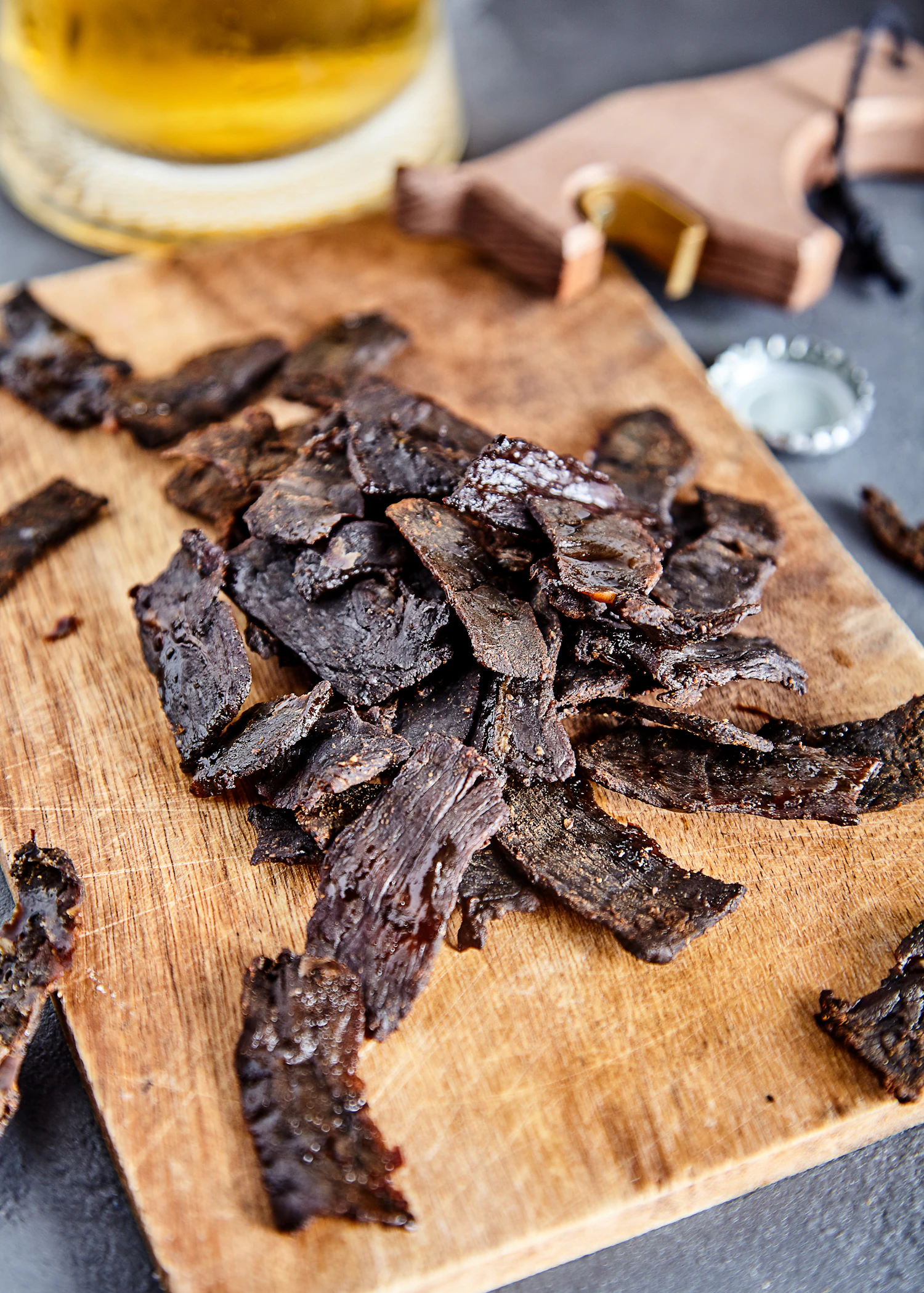 Dark strips of peppered beef jerky piled on a scarred wooden cutting board