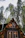 An A-frame cabin is nestled among tall pine trees. The cabin has large triangular windows that allow a glimpse of its warmly lit interior. Strings of lights decorate the cabin's exterior, adding a cozy ambiance.