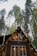An A-frame cabin is nestled among tall pine trees. The cabin has large triangular windows that allow a glimpse of its warmly lit interior. Strings of lights decorate the cabin's exterior, adding a cozy ambiance.