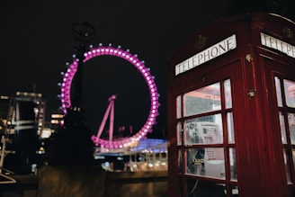 a red telephone booth with a ferris wheel in the background