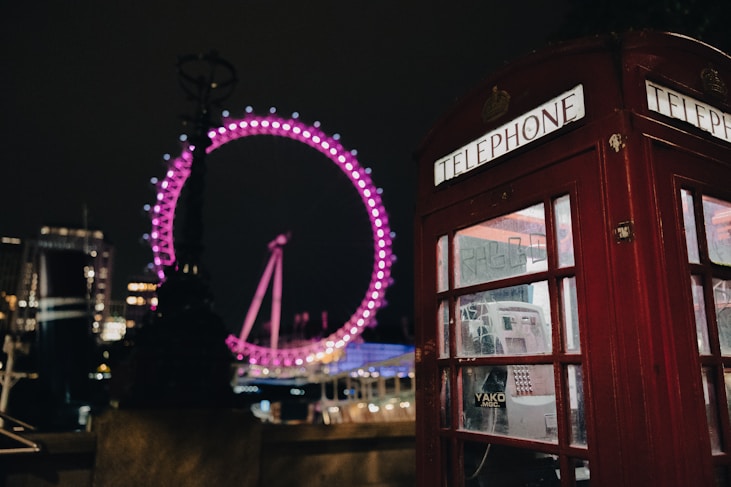 a red telephone booth with a ferris wheel in the background