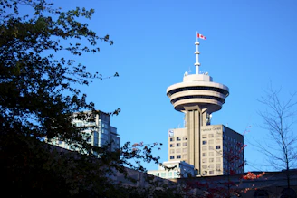 A crisp photo of the iconic CN Tower against a clear blue sky with a subtle maple leaf flag waving nearby.