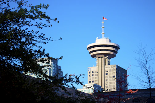 A crisp photo of the iconic CN Tower against a clear blue sky with a subtle maple leaf flag waving nearby.