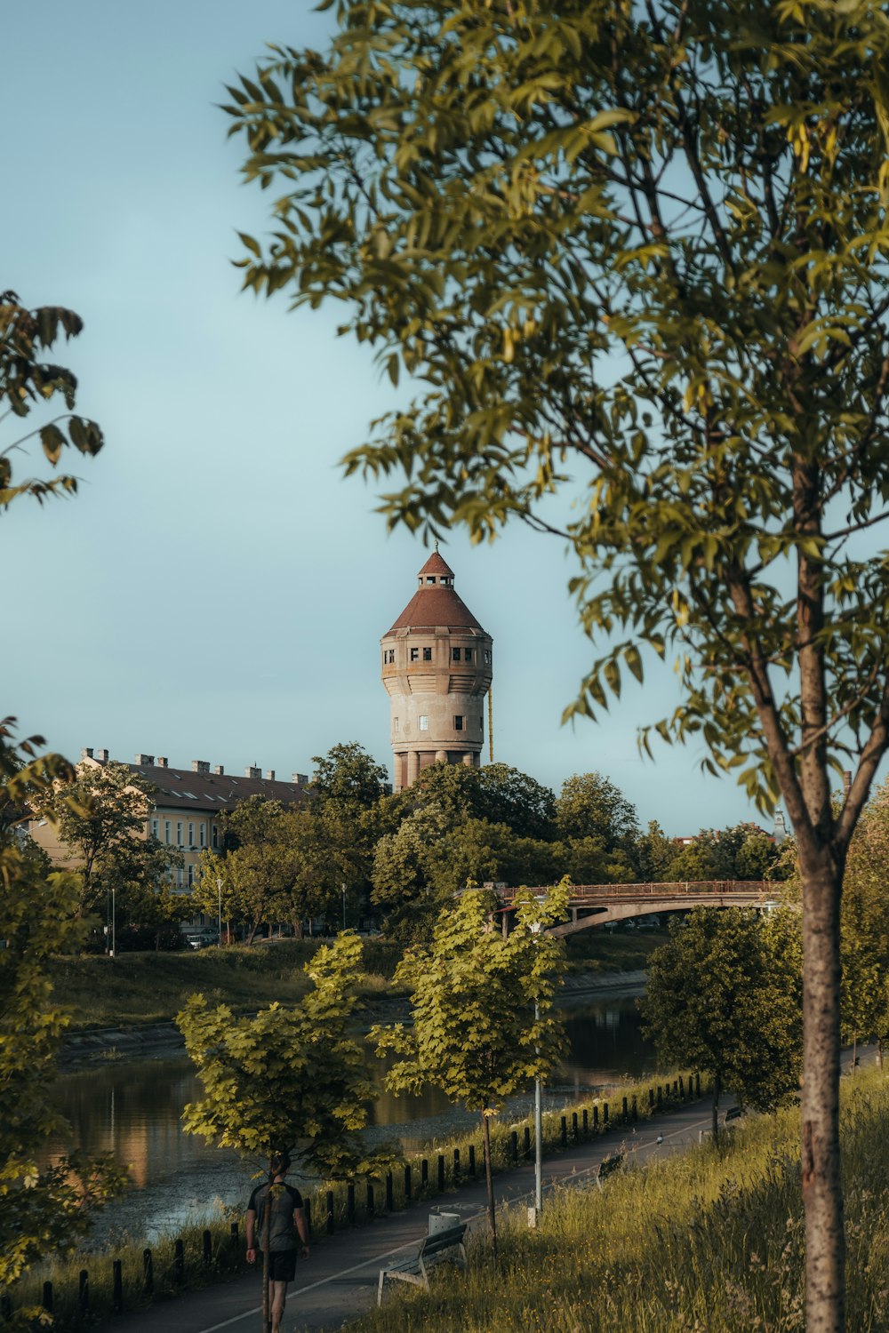 a person walking on a path by a river with a tower in the background