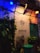 The scene depicts an exterior wall of an establishment named GUDHAAM ANTIQUES & ART. Illuminated by both blue and yellow lights, the wall is adorned with green leafy plants and vintage decorations. A nautical compass decal with cardinal directions is displayed above the business name. There is a turquoise-colored door and some potted plants below.