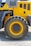 A close-up view of a large, rugged tire attached to a piece of heavy machinery, likely construction equipment. The body of the vehicle is painted bright yellow with some gray elements and appears to be on a gravel surface, suggesting an outdoor, industrial setting.