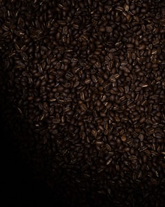 A large pile of dark roasted coffee beans densely packed together, creating a textured surface.