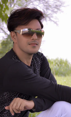 A stylish model wearing oversized sunglasses posing outdoors with greenery behind.