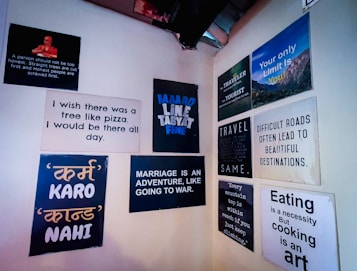 A wall displays various motivational and humorous quotes on individual posters. The messages range from thoughts on travel, marriage, and cooking, to humorous takes on food and personal growth. Some quotes include references to adventure, honest living, and achieving challenging goals.