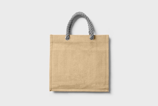 A plain beige tote bag with a textured surface, featuring a sturdy handle made of twisted grey rope.