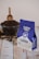A package of Sleepy Owl Original Coffee is prominently displayed in the foreground. The package is colored in blue and white and is labeled as Pure Arabica. Behind the package, there is a glass bowl filled with coffee beans, with a wooden scoop placed upright in the bowl. The scene is set on a wooden surface, enhancing the rustic and cozy atmosphere.