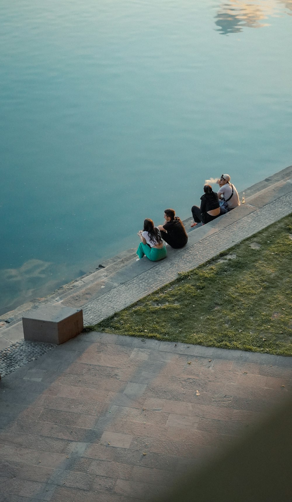a group of people sitting on a stone ledge by a body of water
