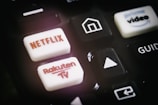 A close-up of a remote control featuring buttons for various streaming services, including Netflix and Rakuten TV, along with other navigational buttons.