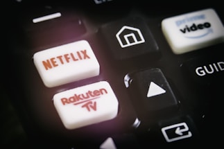 A close-up of a remote control featuring buttons for various streaming services, including Netflix and Rakuten TV, along with other navigational buttons.