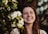 a woman smiling with flowers in the background