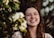 a woman smiling with flowers in the background