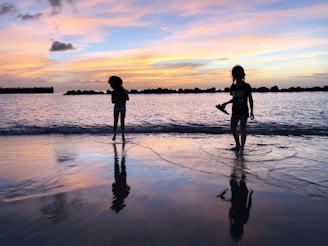 A playful splash between siblings near a tide pool reflecting the sunset colors.