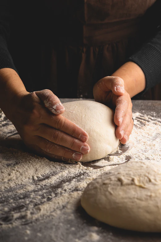 Floured hands shaping a ball of dough