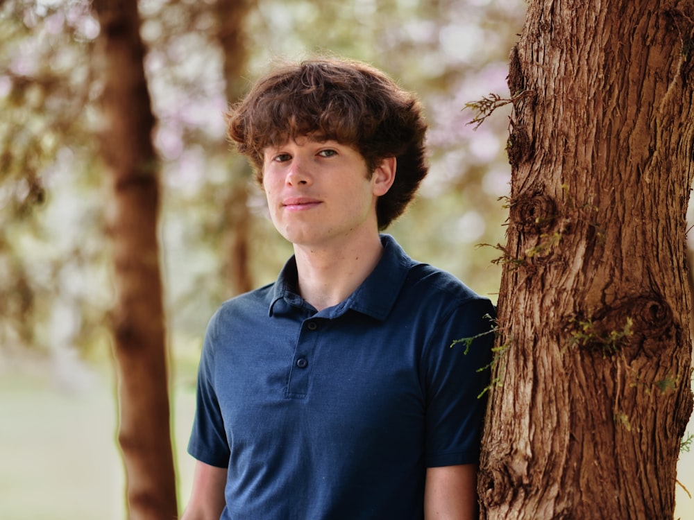 a boy standing next to a tree