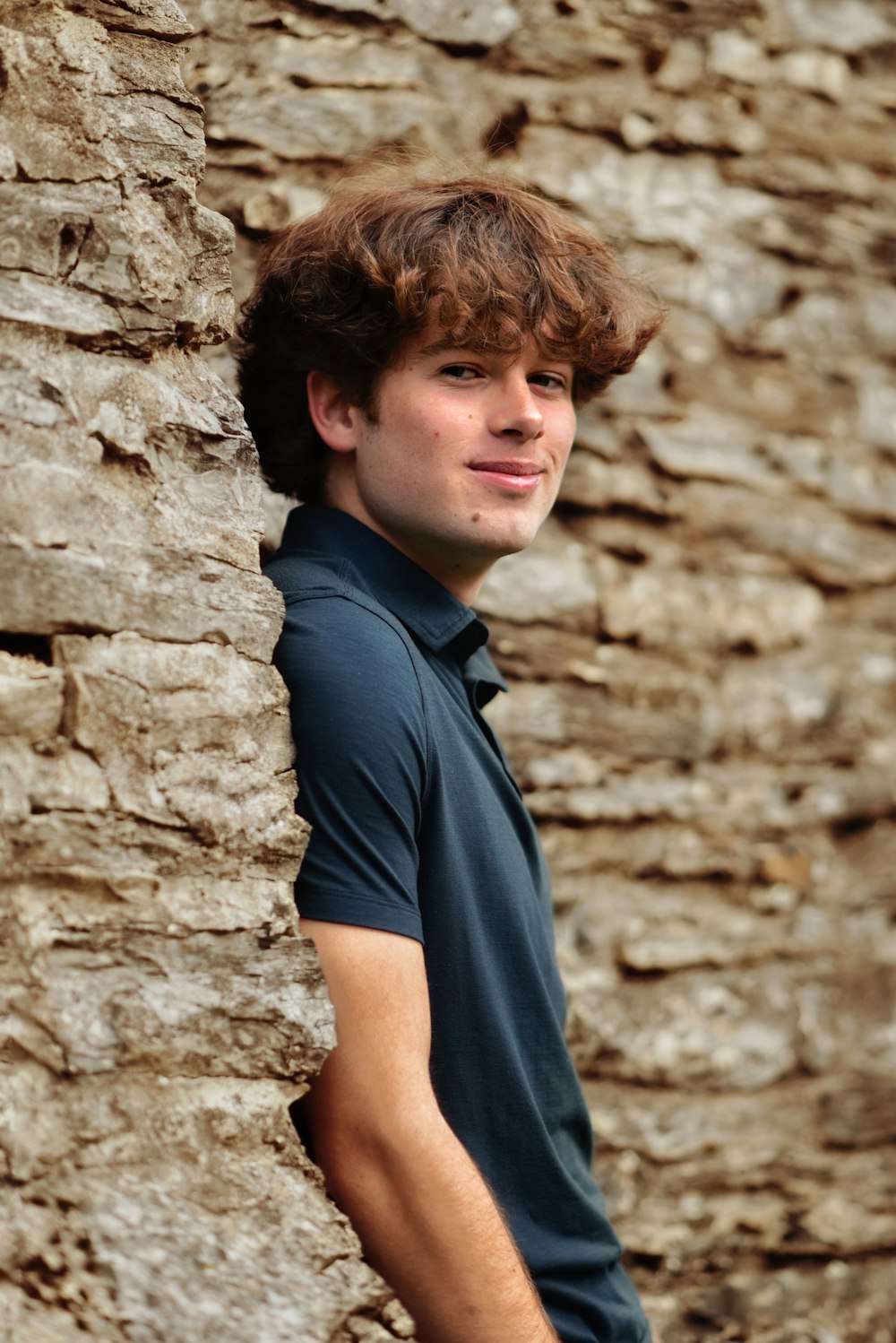 a boy leaning against a rock wall