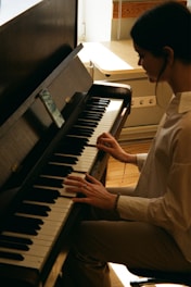 A person is playing the piano with focused attention, framed in soft lighting. The scene appears to be indoors with sunlight streaming through a window, creating a peaceful and intimate atmosphere.