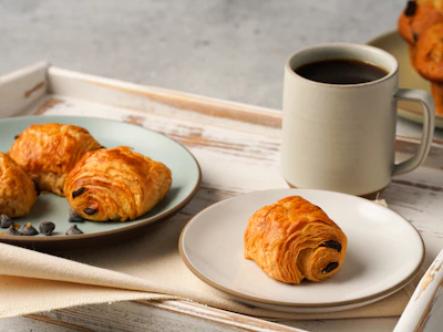 Freshly brewed coffee steaming beside a plate of golden-brown, flaky pastries.
