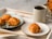A steaming cup of coffee placed on a wooden table next to a small plate of pastries.