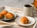 A steaming cup of coffee placed on a wooden table next to a small plate of pastries.