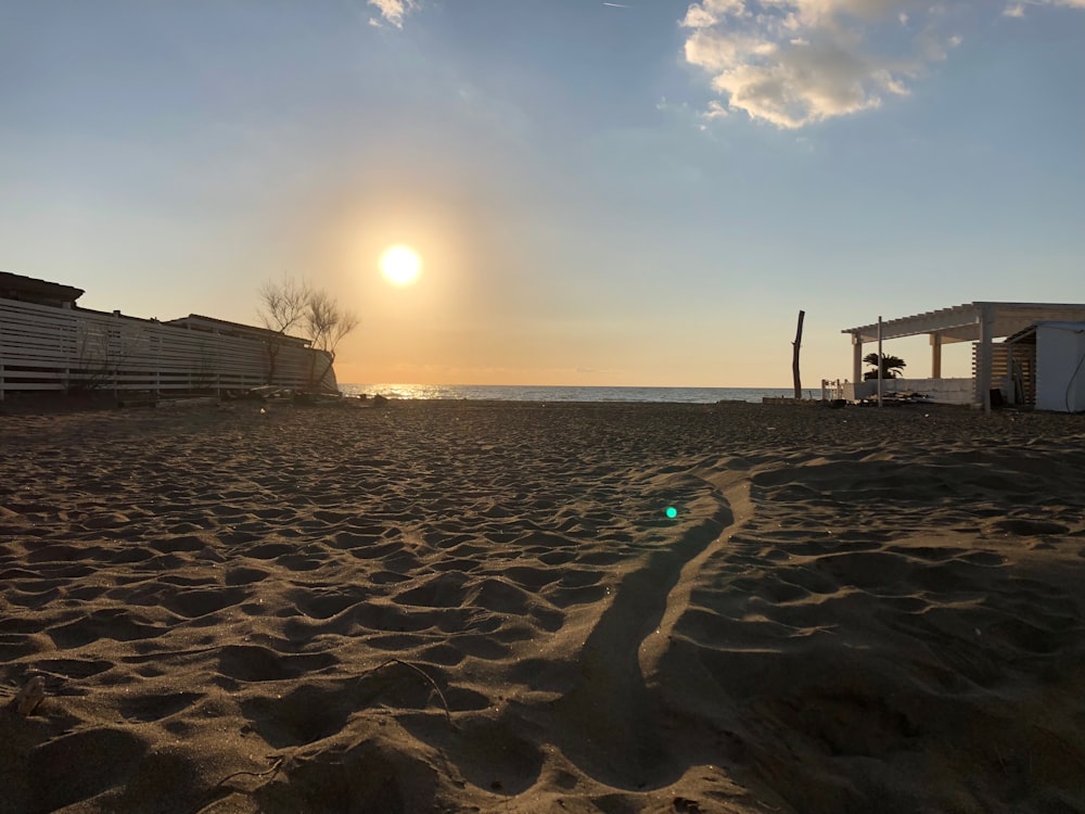 a sandy beach with buildings and the sun in the background