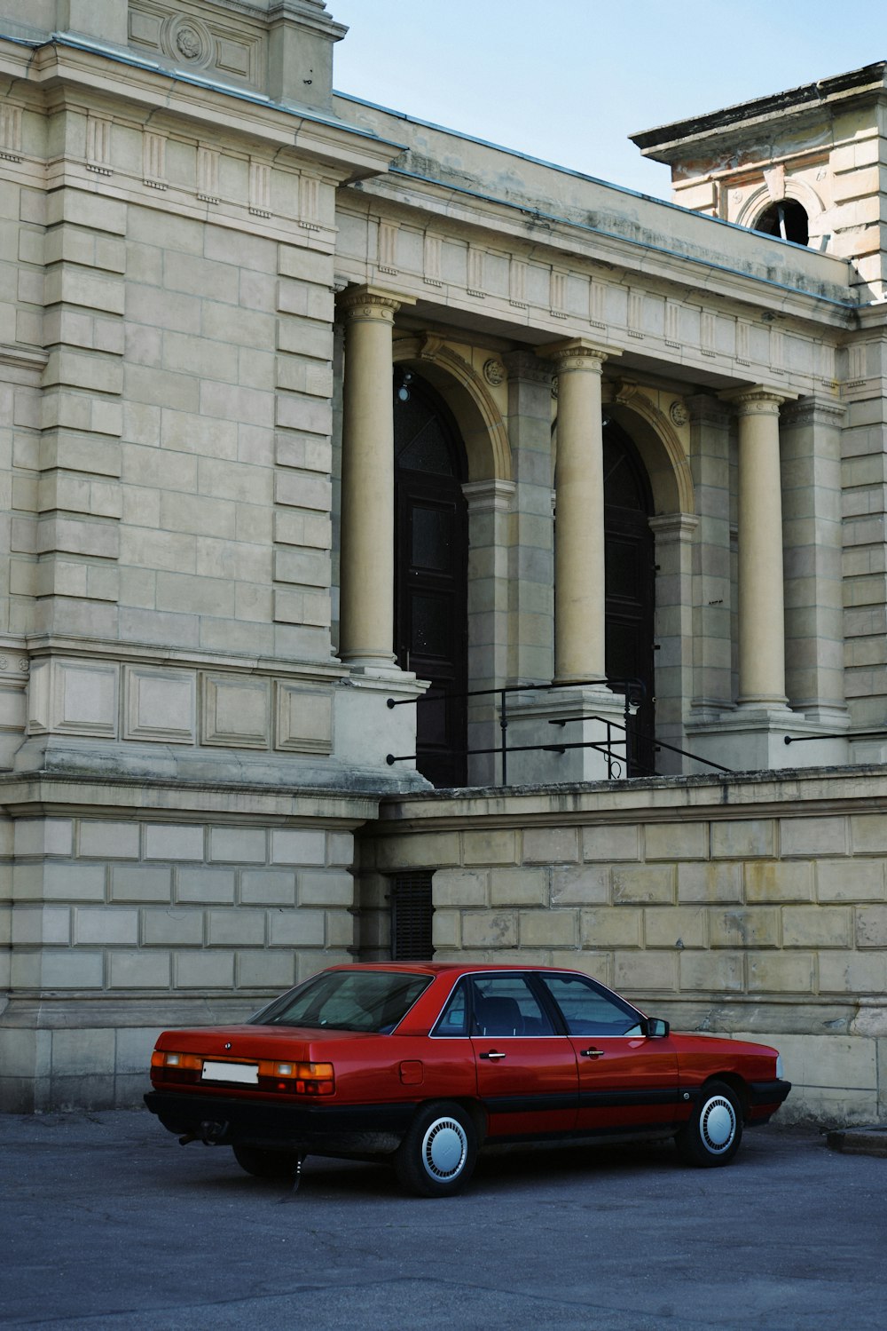 a red car parked in front of a building with columns