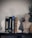 A shelf displays a collection of books on pharmacology, flanked by two white statue bookends in the shape of classical heads and a stone bust of a classical figure. A small green plant in a woven basket adds a touch of natural color.