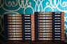 Two stacks of books are arranged, each book with a title that reads 'Team Lead Succeed.' The author's name, Nick Fewings, is visible on the spines. The books are neatly placed on a wooden surface, in front of a decorative background with intricate teal and cream patterns.