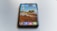 A smartphone is placed on a smooth, light-colored surface. The phone displays a scenic mountain landscape as the wallpaper. Several browser app icons, including Edge, Safari, Chrome, Firefox, and Brave, are visible on the screen.