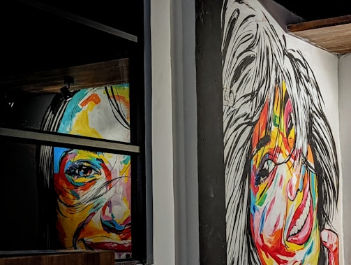 Two colorful, abstract portraits cover the walls, with vivid brushstrokes creating expressive faces. Bold, contrasting colors enhance the lively nature of the portraits, which seem to capture a sense of motion and emotion.