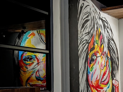 Two colorful, abstract portraits cover the walls, with vivid brushstrokes creating expressive faces. Bold, contrasting colors enhance the lively nature of the portraits, which seem to capture a sense of motion and emotion.