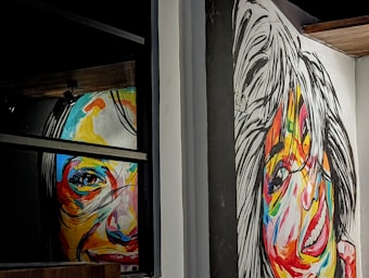 Two colorful, abstract portraits cover the walls, with vivid brushstrokes creating expressive faces. Bold, contrasting colors enhance the lively nature of the portraits, which seem to capture a sense of motion and emotion.