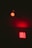 A red neon sign with the word 'GIRLS' repeated three times is illuminated against a dark background. Above it, there is a single red light bulb casting a red glow.