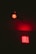 A red neon sign with the word 'GIRLS' repeated three times is illuminated against a dark background. Above it, there is a single red light bulb casting a red glow.