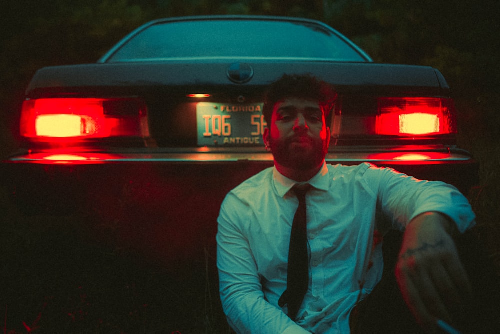 a man in a tie and tie standing in front of a car