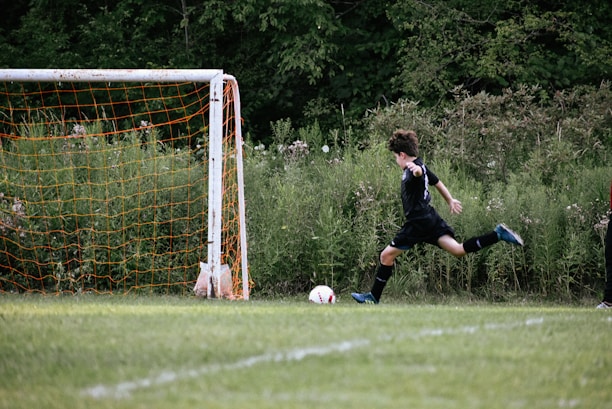 Player aiming a powerful kick towards vertical hoops arranged in front of a soccer goal.