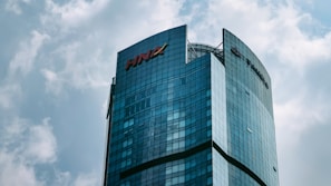 A modern skyscraper with a curved glass facade, prominently displaying the HNA logo at the top. The building rises against a backdrop of a cloudy sky, showcasing a blend of architectural innovation and corporate branding.