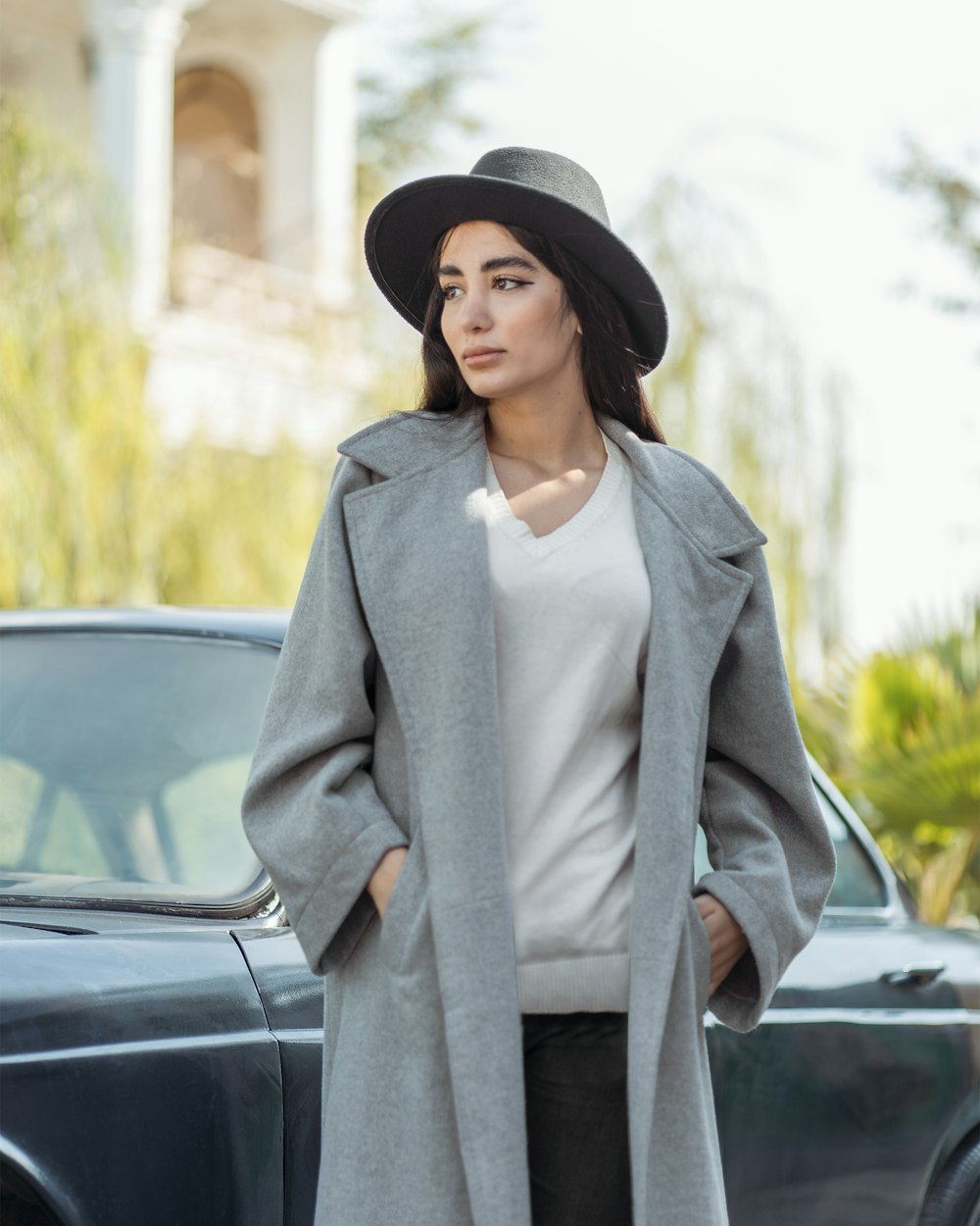 uma pessoa em um casaco cinza e chapéu de pé ao lado de um carro