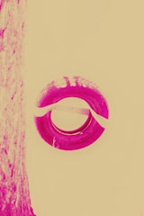 A stylized image featuring a circular tire with visible tread patterns in a vivid magenta hue against a pale yellow background. The left side shows a textured vertical surface that is similarly colored.