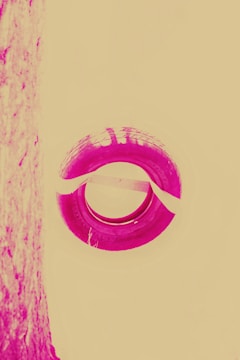 A stylized image featuring a circular tire with visible tread patterns in a vivid magenta hue against a pale yellow background. The left side shows a textured vertical surface that is similarly colored.
