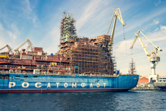 A skilled technician inspecting a ship's engine in a busy shipyard under clear skies.