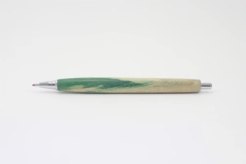 Close-up of a deep carmine red pen resting on crisp parchment with matte forest green accents.