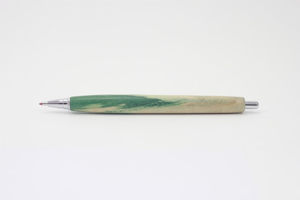 Handcrafted ballpoint pen embedded with tiny dried petals, lying on a simple white desk.
